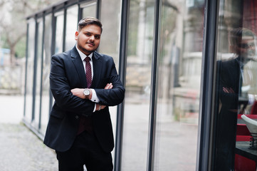 Stylish indian businessman in formal wear standing against windows in business center.