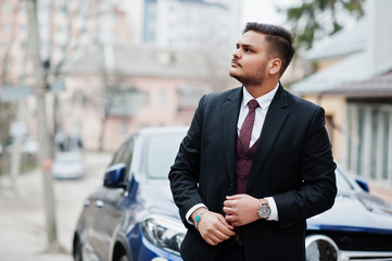 Rich indian businessman in formal wear standing against business suv car.