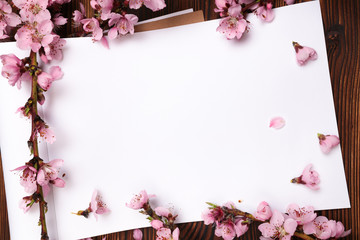White paper sheet and sprigs of the apricot tree with flowers on wooden background. Place for text. The concept of spring came, happy easter, mother's day.Top view.Flay lay. Copy space.