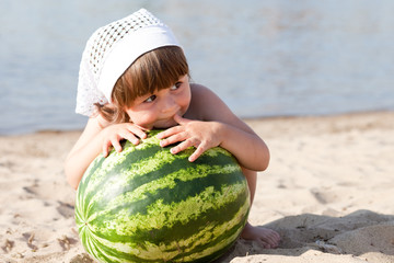 Fototapeta premium Little girl with a round watermelon on the beach