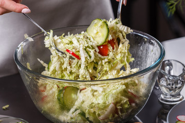 a young woman in a gray apron mixes a salad of Chinese cabbage
