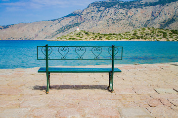 Naklejka na ściany i meble Metal green bench on the waterfront with sea and mountain view