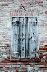Window shutter of rural house, with brick wall and ancient stones.