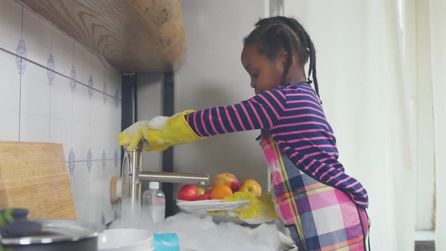 Happy little girl washing the dishes in the kitchen