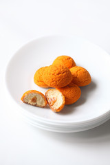 Choux Buns with Craquelin (crispy cream puffs) filled with tropical cream and salted caramel sauce, on white plate, on white background.