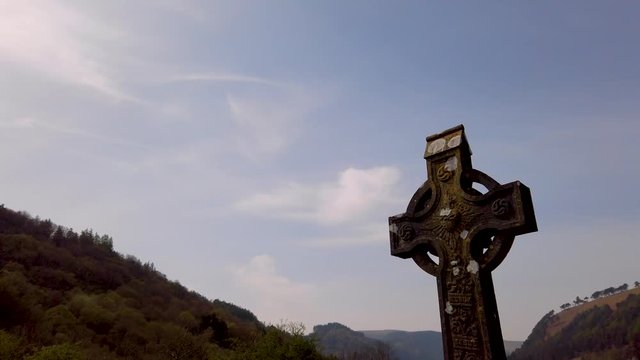 Tilt camera down on a large Irish Celtic rock cross in the middle of a cemetery.
