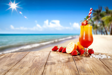 Fresh cold drink on wooden table and free space for your decoration. Summer blurred background of beach and palms with ocean landscape and sun . 