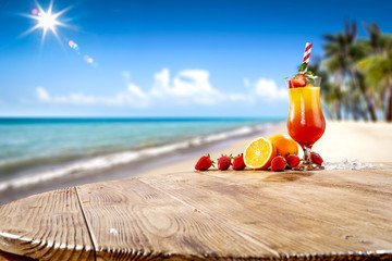 Fresh cold drink on wooden table and free space for your decoration. Summer blurred background of beach and palms with ocean landscape and sun . 