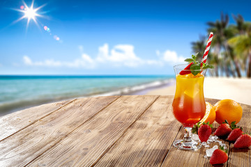 Fresh cold drink on wooden table and free space for your decoration. Summer blurred background of beach and palms with ocean landscape and sun . 