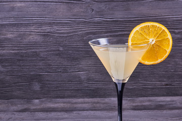 Goblet martini with fresh orange juice and orange slice, on a dark wooden background.