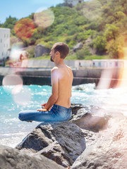 relaxed young man meditating while sitting on the beach