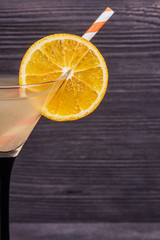 Orange slice on the edge of the martini glass and a cocktail tube, on a dark wooden background. Close-up