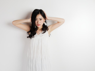 Naklejka premium Portrait of beautiful Chinese woman in sexy white dress posing with white wall background, young girl puts her hands on her head and looks worried.