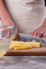 young woman in an apron cuts potatoes