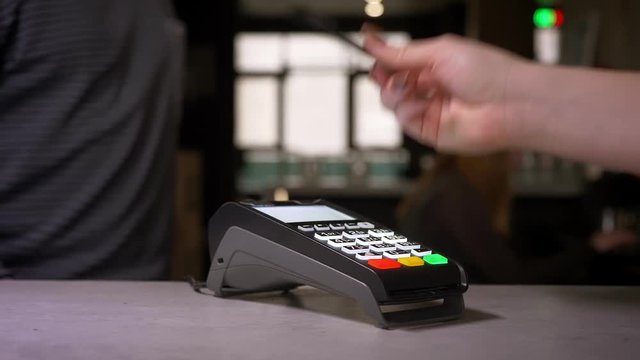 Close-up shot of woman using terminal and credit card performs contactless paypass payment.