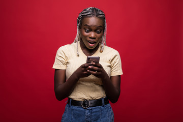 Happy young african woman use mobile phone casually dressed standing isolated over red background