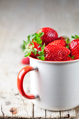 Organic red strawberries in white ceramic cup on rustic wooden background.