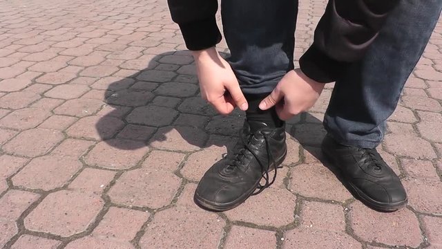 A man tying shoelaces on shoes walking in the park in summer