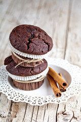 Fresh dark chocolate muffins with cinnamon sticks on white plate.