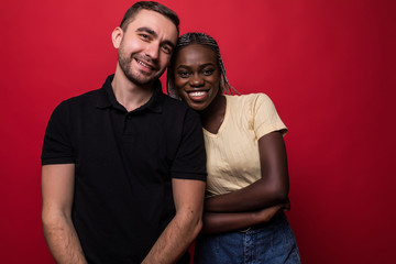 Obraz premium Portrait of a smiling young interracial couple hugging and looking at camera isolated on the red background