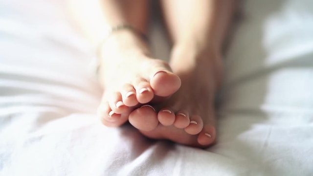 Arthritis disease in the elderly, old and young people. Foot massage on the bed, a great pedicure. Foot fatigue after a hard day and relaxing massage. A woman rubs the bottom of his tired, sore foot.