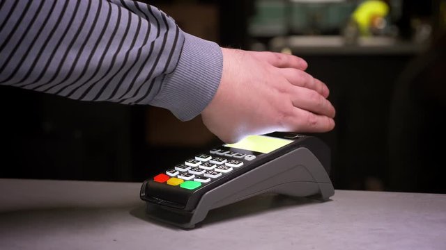 Close-up shot of man attaches hand with microchip implant to terminal making successful contactless payment on gym background.