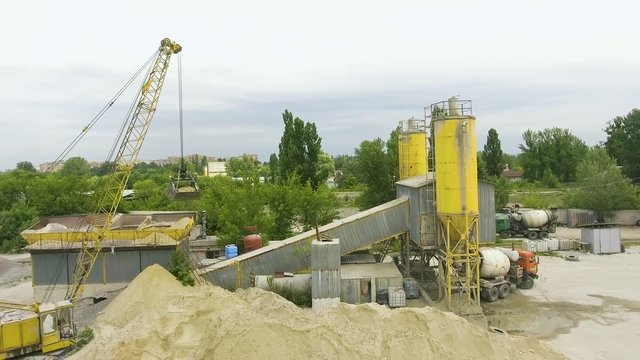 arc shot of crane claw loading sand into conveyor at concrete factory