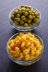 canned corn and green peas in a glass bowl on a dark stone background