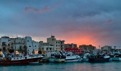 Fototapeta premium Monopoli, Puglia, Italy - April 07, 2019: sunset on the old town harbor with fishing ships and vessels in the internal dock