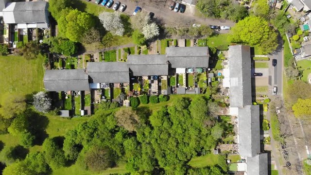 Top down view moving left over a residential area comprising of mid terrace houses with woodlands at the rear in Basildon on a sunny day
