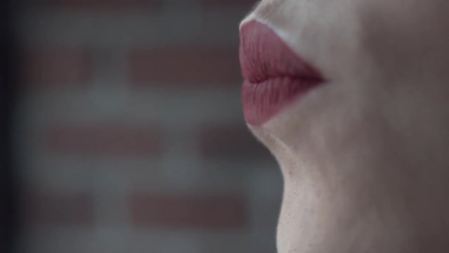 Close-up of woman's face and lips which are covering with bright red lipsticks. Action. Fashion and colors