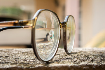 A pair pf round glasses on a rough surface under the sun in a garden.