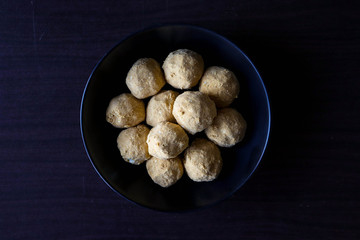 ladoo an Indian sweet dish witch is made from chickpeas flour and sugar powder,these are in a bowl which is on a dark wooden table 