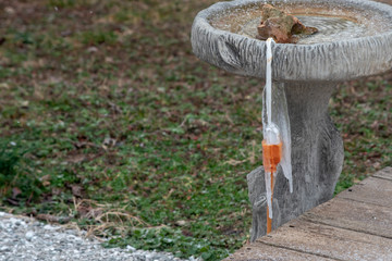 Rain water has frozen over the electrical outlet of a power source and extension cord on this outdoors birdbath in the winter. Bokeh effect.