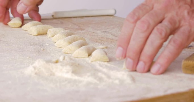 Mani di un uomo stanno tagliando il cordone di impasto per fare gli gnocchi di patate in casa su un tagliere di legno. Vista dall'alto.
