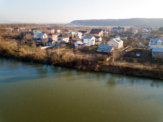 Fototapeta na wymiar Aerial top view, countryside panorama of residential houses on river bank on blue sky and woody hill background. Drone photography.