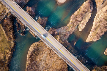Aerial view of white bridge with moving car over blue water and stony islands.