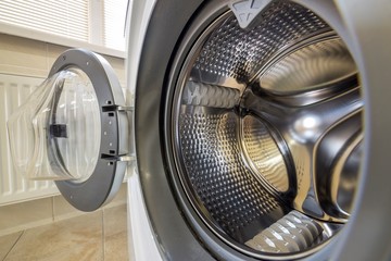 Close-up detail of modern washing machine interior with open door interior. Silver shiny stainless...