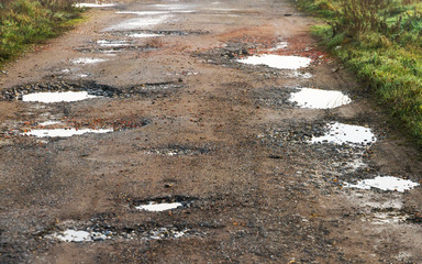 Baches con agua de lluvia en camino asfaltado  deteriorado