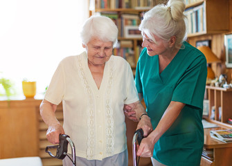 Nursing assistant helping senior woman with walking frame