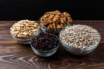 Sunflower seeds, salted peanut, walnut and raisins on dark wooden background.