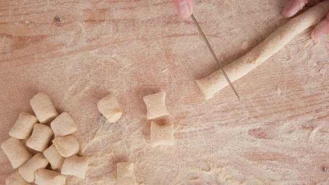Mani di un uomo stanno tagliando il cordone di impasto per fare gli gnocchi di patate in casa su un tagliere di legno. Vista dall'alto.
