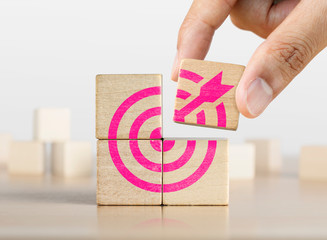 Hand putting the last piece of wooden blocks with the dart target icon. Goal, business goal,...