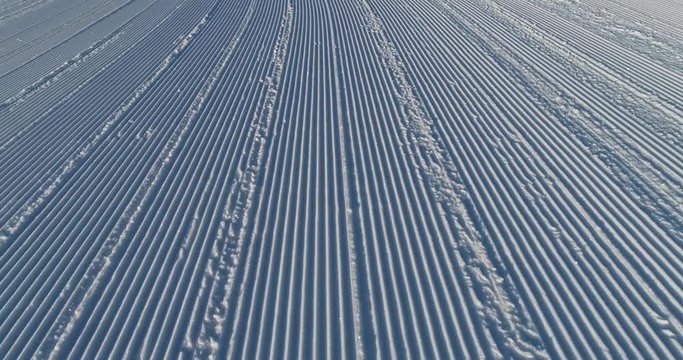 Flying over the ski slope on a frosty sunny day. Ski velvet, snow sparkles. Smooth parallel lines texture. 4K drone footage