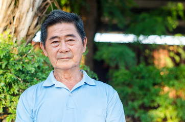 Happy asian senior gentleman sitting on a wooden bench and relaxing in a park  on a sunny day