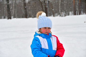 Obraz premium funny little girl playing with snow. child with snowball on a walk in the winter. Kids play outside. Winter fun concept.