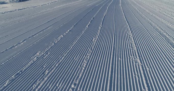 Flying over the ski slope on a frosty sunny day. Ski velvet, snow sparkles. Smooth parallel lines texture. 4K drone footage