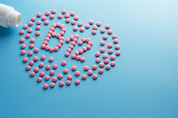 Pink tablets in the form of B12 in the heart on a blue background, spilled from a white can.