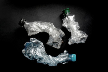 Flattened empty used plastic PVC bottles on black background. Crumpled bottle - recycle eco concept.