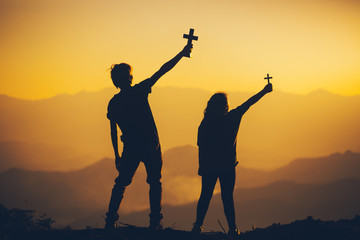 Young male and girl standing holding christian cross at sunset background. christian silhouette concept.